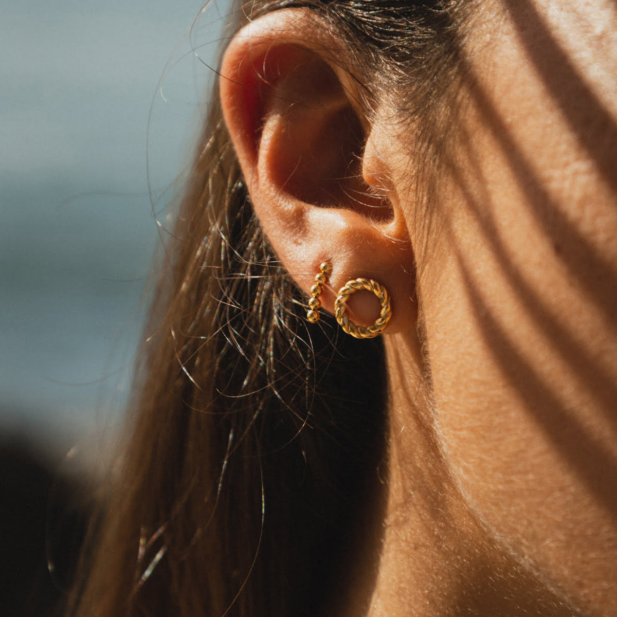 Close-up of a woman's ear wearing gold earrings. Jewelry from AN JEWELS JEWELRY Mod. AL.EMW02Y.