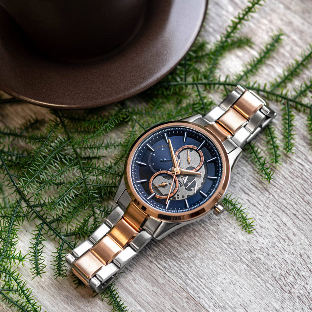 Elegant ARMANI EXCHANGE Mod. AX1874 wristwatch with SS IP rose gold case and bracelet, displayed on a wooden surface with greenery.