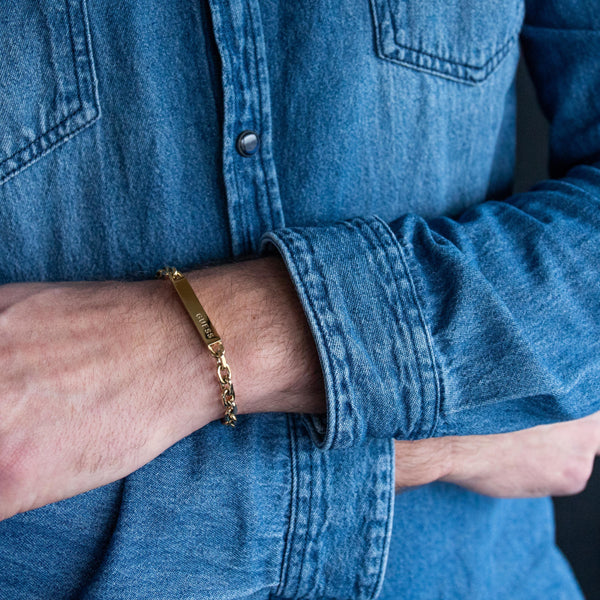 Man wearing denim shirt with GUESS JEWELS JEWELRY Mod. JUXB03000JWYGS bracelet on wrist.