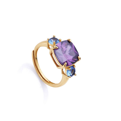 Elegant gold ring with a large purple gemstone and two smaller blue gems on a white background, emphasizing luxury and style.