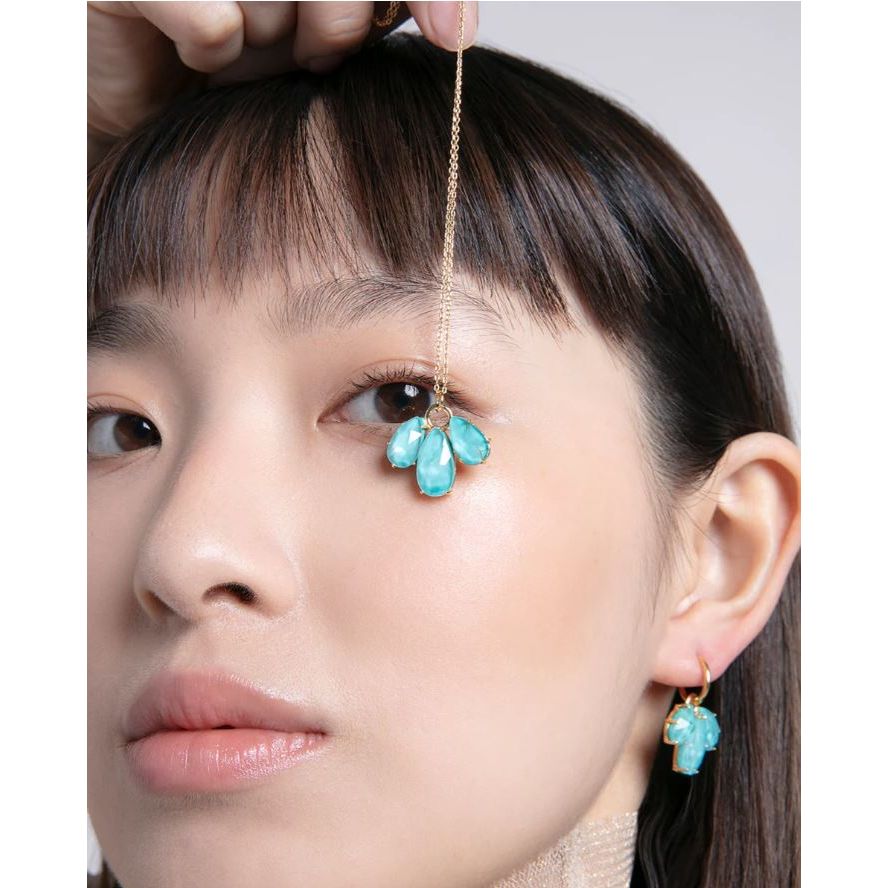 Woman modeling turquoise gemstone necklace and matching earrings, close-up.