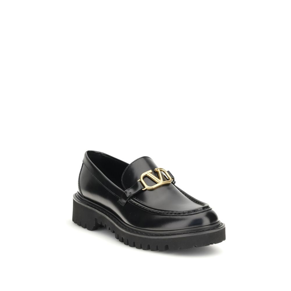 Valentino Garavani Black Leather Slip-On Loafers with brass VLogo detail and rubber lug sole, showcasing elegance and modern design.