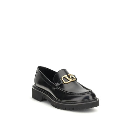 Valentino Garavani Black Leather Slip-On Loafers with brass VLogo detail and rubber lug sole, showcasing elegance and modern design.