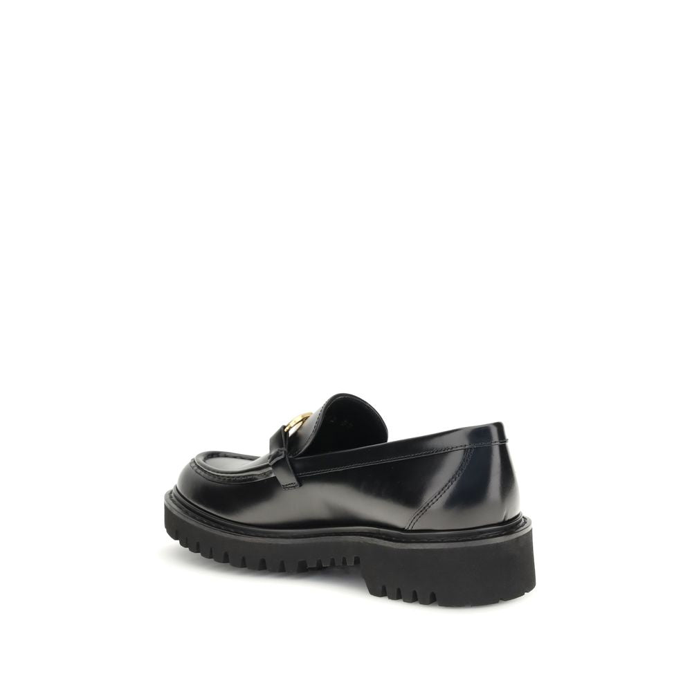 Valentino Garavani Black Leather Slip-On Loafers with brass VLogo and rubber lug sole, showcasing a side view for AW25 fashion collection.