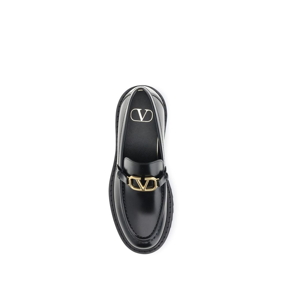 Valentino Garavani Black Leather Slip-On Loafers with VLogo and antique brass finish, featuring rubber lug sole for stability and comfort.