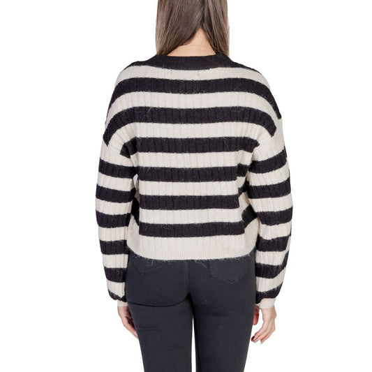 Woman wearing black and white striped knitted sweater, viewed from the back, with casual black pants.